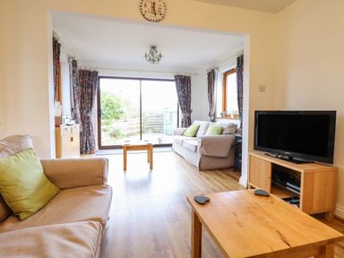 A living room with two beige sofas and green cushions a wooden coffee table a television on a wooden stand and sliding glass doors at Dehangfa in Fairbourne