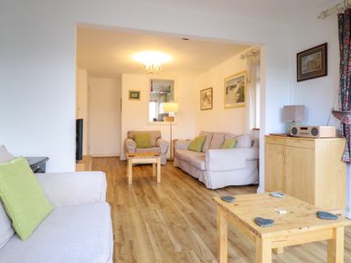 A living room with beige sofas green cushions wooden tables and a wooden cabinet at Dehangfa in Fairbourne
