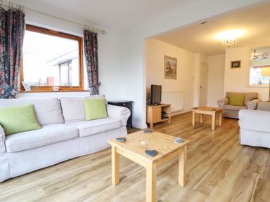 A living room with sofas wooden tables a television and a window with curtains at Dehangfa in Fairbourne