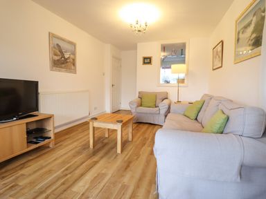 A living room with gray sofas and green cushions a wooden coffee table a TV on a wooden stand and framed pictures on the walls at Dehangfa in Fairbourne