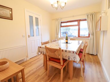 A dining room with a table covered in a patterned cloth surrounded by six wooden chairs at Dehangfa in Fairbourne