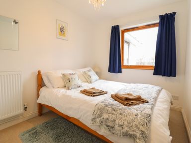 A bedroom with a double bed with cushions and towels a window with blue curtains and a small lamp at Dehangfa in Fairbourne