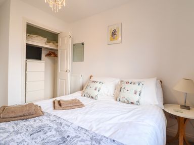 A bedroom with a bed with pillows and towels a nightstand with a lamp and an open closet with a chest of drawers at Dehangfa in Fairbourne