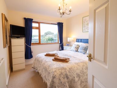 A bedroom with a bed with folded towels a chest of drawers a television and a window with blue curtains at Dehangfa in Fairbourne