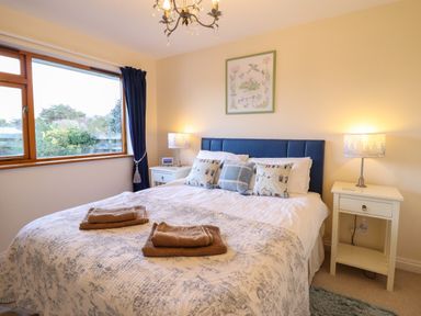 A bedroom with a large bed with pillows and folded towels on the bed two bedside tables with lamps and a window with blue curtains at Dehangfa in Fairbourne