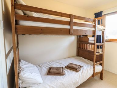 A bedroom with a wooden bunk bed with white bedding and two brown towels on the bottom bed next to a window at Dehangfa in Fairbourne