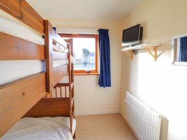 A bedroom with wooden bunk beds a window with blue curtains a wall-mounted television and a radiator at Dehangfa in Fairbourne