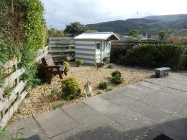 A garden area with a small shed a wooden bench plants gravel and a small dog at Dehangfa in Fairbourne