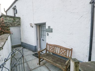 An outdoor area with a wooden bench a door with shutters and a sign reading Kirkstone Cottage in Ambleside
