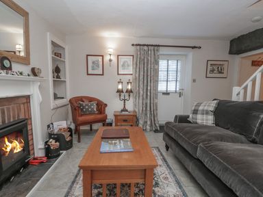A living room with a fireplace a wooden coffee table a sofa an armchair and a door at Kirkstone Cottage in Ambleside