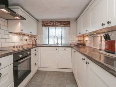 A kitchen with white cabinets a stovetop an oven a sink and a window at Kirkstone Cottage in Ambleside