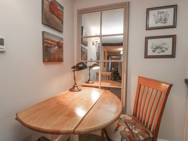A wooden table with a lamp and a wooden chair with a patterned cushion in front of a mirror on a wall at Kirkstone Cottage in Ambleside