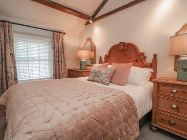 A bedroom with a wooden bed frame side tables lamps and a window with floral curtains at Kirkstone Cottage in Ambleside