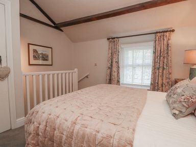 A bedroom with a bed covered in a quilt near a window with curtains and a bedside table lamp at Kirkstone Cottage Ambleside