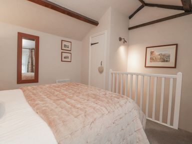 A bedroom with a bed covered with a blanket a mirror on the wall framed pictures a door and a railing at Kirkstone Cottage Ambleside