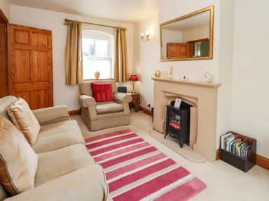 A living room with a beige sofa and armchair a fireplace and a striped rug at Elder Cottage in Mickleton near Chipping Campden