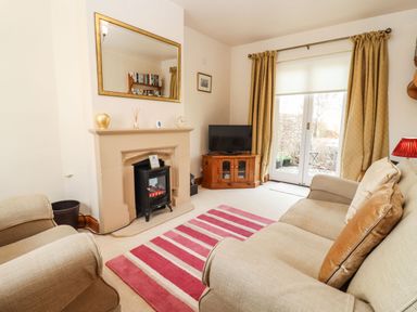 A living room with a fireplace a television on a wooden cabinet and a striped rug at Elder Cottage in Mickleton near Chipping Campden