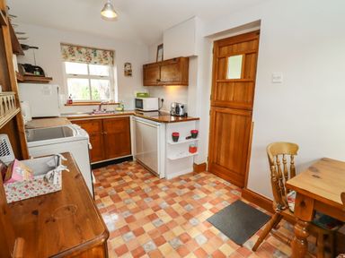 A kitchen with wooden cabinets tiled floor and a wooden door at Elder Cottage in Mickleton near Chipping Campden
