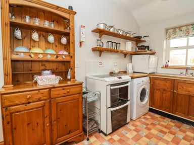 A kitchen with wooden cabinets a stove a washing machine a microwave and a wooden cupboard holding cups and plates at Elder Cottage Mickleton near Chipping Campden