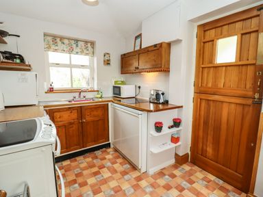 A kitchen with wooden cabinets a white stove a refrigerator a microwave and a wooden door at Elder Cottage in Mickleton near Chipping Campden