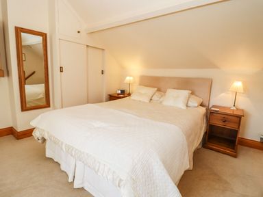 A bedroom with a double bed bedside tables lamps and a wall mirror at Elder Cottage in Mickleton near Chipping Campden