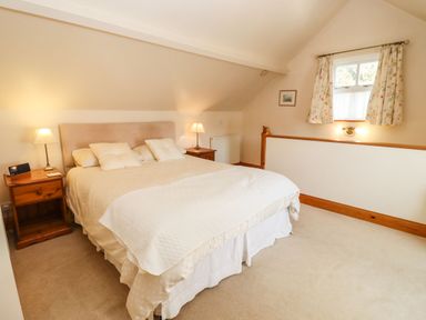A bedroom with a double bed pillows two bedside tables lamps a window with curtains and a framed picture at Elder Cottage in Mickleton near Chipping Campden