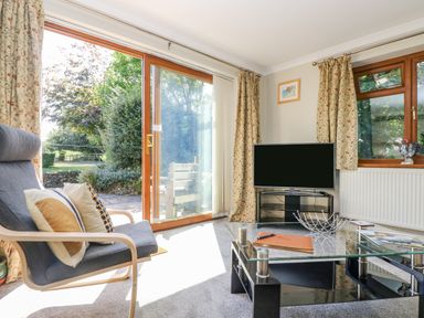 A sitting room with a chair and cushions a glass coffee table and a television near sliding glass doors at Manege Cottage Near St Agnes