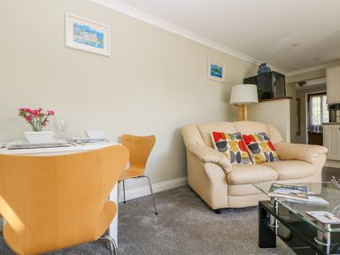 A dining table with two wooden chairs and a beige sofa with patterned cushions in a living room at Manege Cottage Near St Agnes