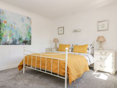 A bedroom with a white metal bed frame orange bedding two bedside tables with lamps and paintings on the walls at Manege Cottage Near St Agnes