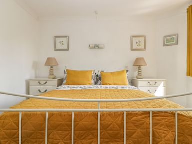 A bedroom with a bed with yellow bedding and pillows two bedside tables with lamps and framed pictures on the wall at Manege Cottage Near St Agnes