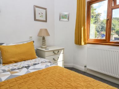 A bedroom with a bed a nightstand lamp two pictures and a window with yellow curtains at Manege Cottage Near St Agnes
