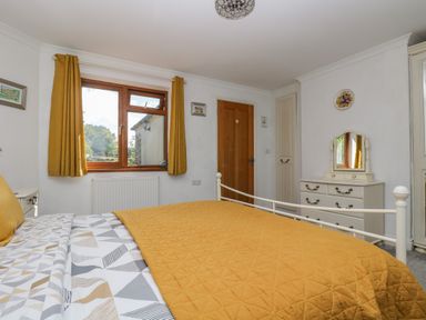 A bedroom with a bed yellow bedding white dresser with mirror wooden door and window with yellow curtains at Manege Cottage Near St Agnes