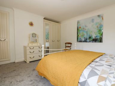 A bedroom with a bed covered with a yellow quilt a dresser with a mirror a wooden chair and a wardrobe with mirrored doors at Manege Cottage Near St Agnes