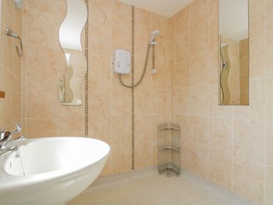 A bathroom with a white sink a shower area with a showerhead and wire rack on tiled walls at Manege Cottage Near St Agnes