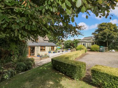An outdoor view of a garden with trimmed hedges trees and a gravel driveway near buildings at Manege Cottage Near St Agnes