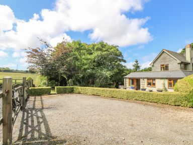 A gravel driveway next to a house with hedges and trees near a field at Manege Cottage Near St Agnes