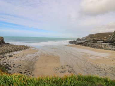A beach with sand and rocks bordered by cliffs and grass near the ocean at Manege Cottage Near St Agnes