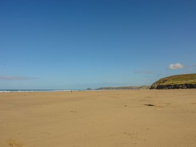 A wide sandy beach with a few people near the water and cliffs in the distance at Manege Cottage Near St Agnes