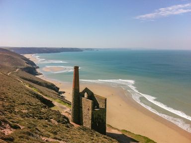 A coastal landscape with an old stone building and chimney near a sandy beach and blue sea at Manege Cottage Near St Agnes
