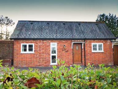 A brick house with a wooden door and multiple windows with a hedge in front at South Lodge in Hazelbury Bryan