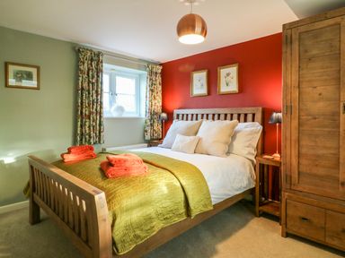 A bedroom with a wooden bed and wardrobe green and red walls and folded towels on the bed at South Lodge in Hazelbury Bryan
