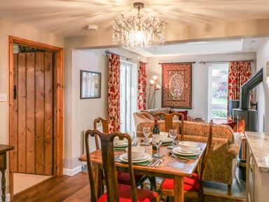 A dining table set with plates glasses and cutlery next to a sitting area with sofas a rug on the wall and a stove with a chimney at South Lodge in Hazelbury Bryan