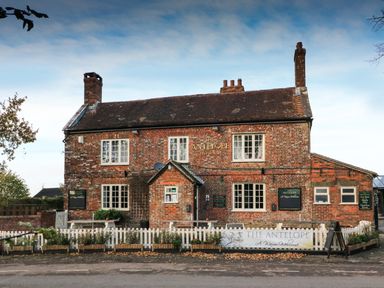 A brick building with white windows and chimneys a white picket fence and signs reading The Antelope outside