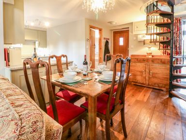 A dining area with a wooden table and four chairs set with bowls and glasses near a kitchen and spiral staircase at South Lodge in Hazelbury Bryan
