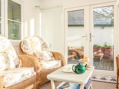 A sunroom with wicker armchairs and a table set with a green teapot cups and cake stand at South Lodge in Hazelbury Bryan