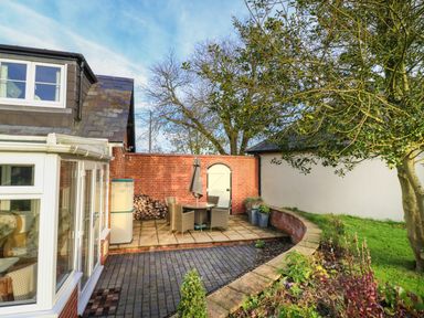 An outdoor patio with a table and chairs under a tree next to a brick wall at South Lodge in Hazelbury Bryan