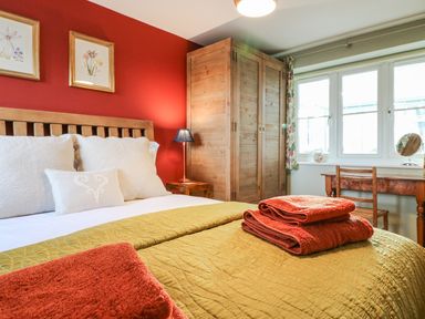 A bedroom with a wooden bed with white pillows and a green quilt towels on the bed a wooden wardrobe a desk and chair by the window at South Lodge in Hazelbury Bryan