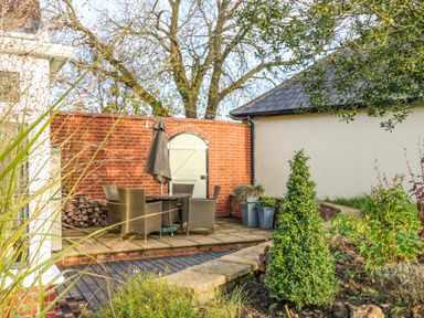 A garden area with a patio table and chairs under an umbrella next to a brick wall and wooden door at South Lodge in Hazelbury Bryan
