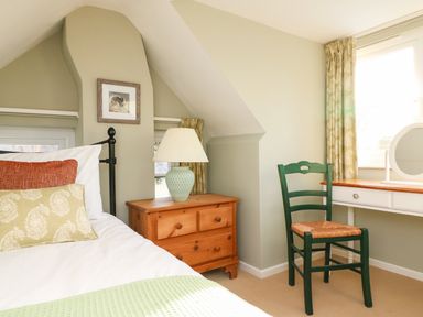 A bedroom with a bed pillows a wooden nightstand with a lamp a green chair and a white desk at South Lodge in Hazelbury Bryan