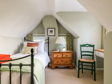 A bedroom with a single metal bed a wooden bedside table with a lamp and a green chair at South Lodge in Hazelbury Bryan